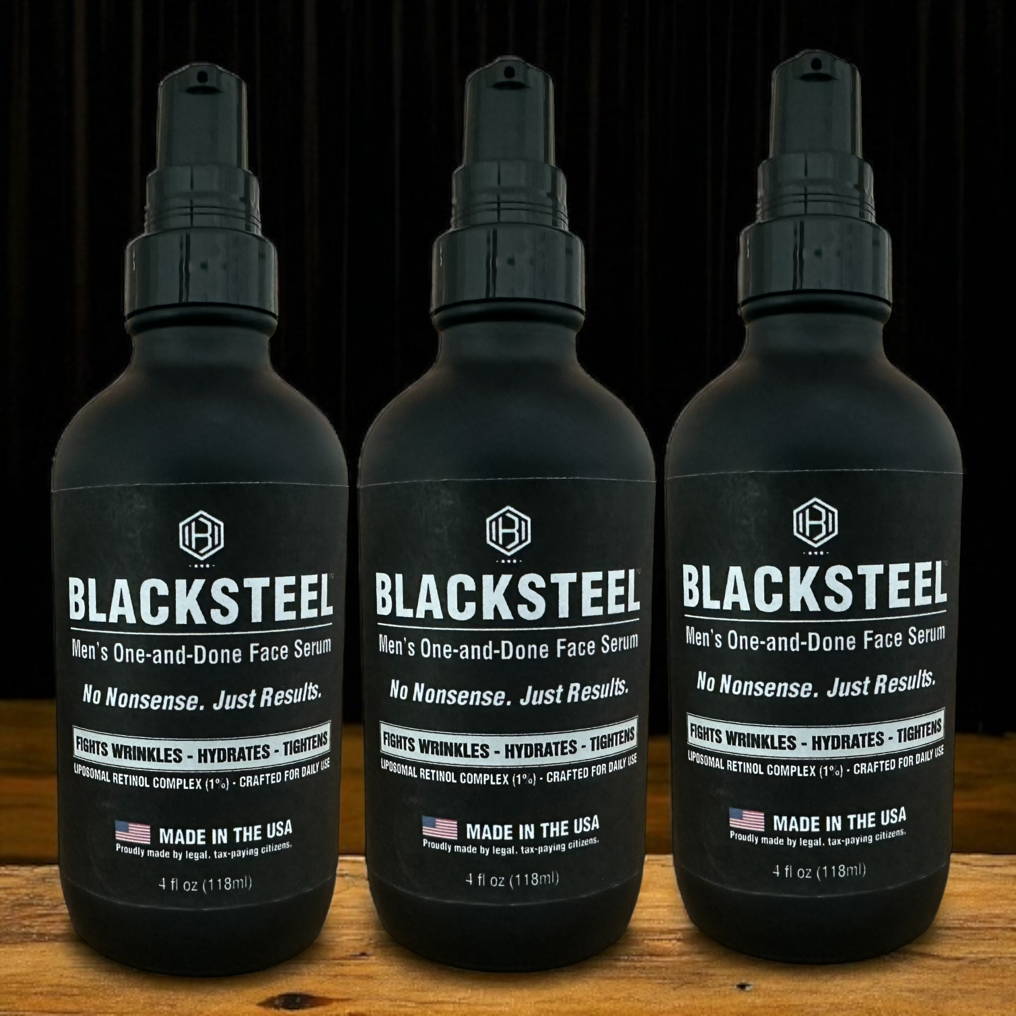 Three bottles of BLACKSTEEL™ face serum standing on wood with matte black packaging — 12 oz men's anti-aging skincare bundle.